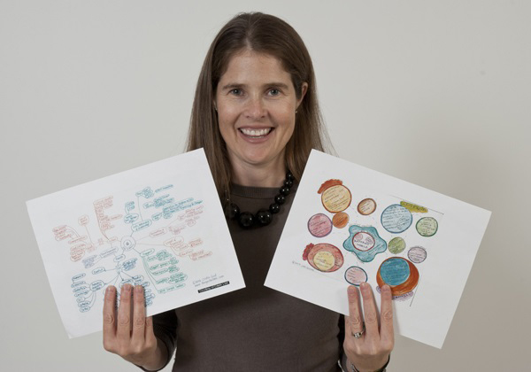 Woman holds two sheets of paper with illustrations and notes on them.