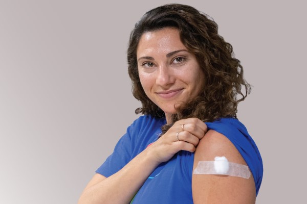 A woman lifts her t-shirt sleeve to show a bandage covering her flu shot injection. 