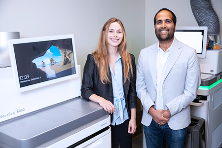 Two clinician scientists stand infront of a clinical RNA sequencer at SickKids.