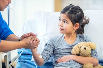 Child seated in hospital bed holding an adult's hand.