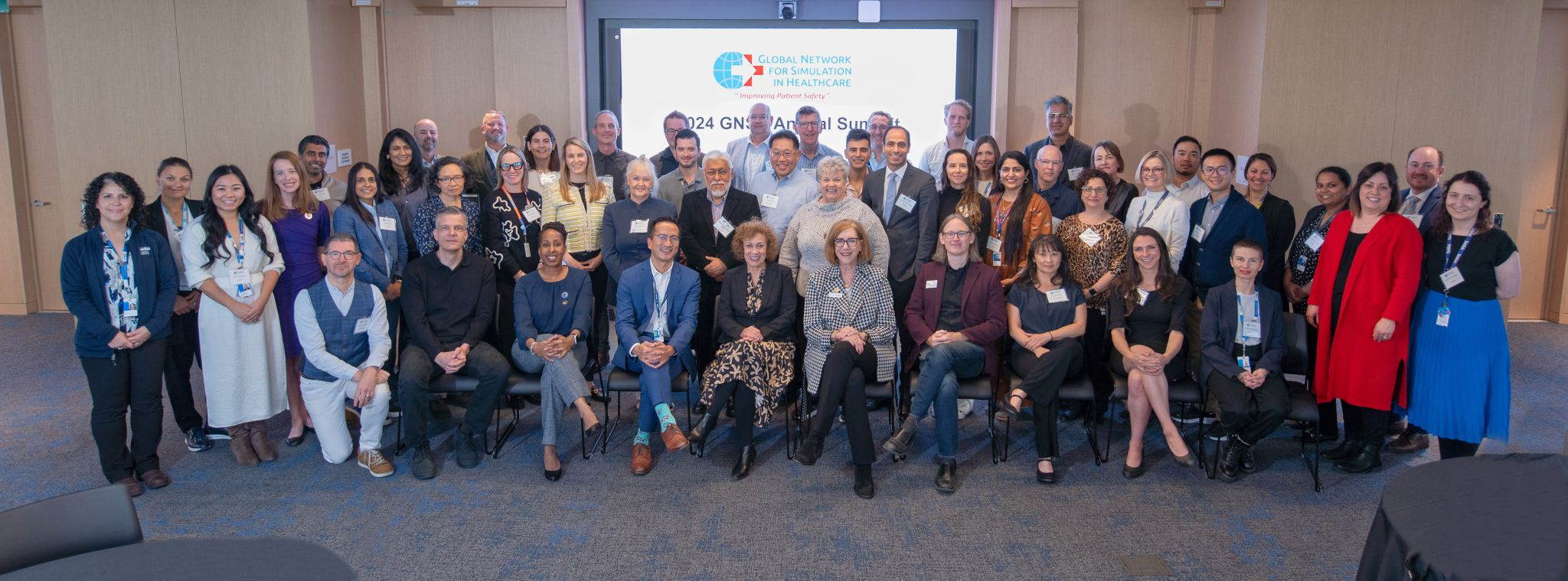 Group photo of approximately 40 individuals in a conference room, dressed in business casual attire.