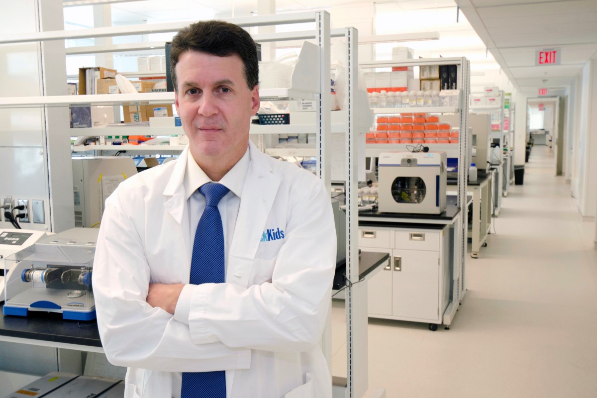 A researcher in a white lab coat standing in a laboratory with scientific equipment. 