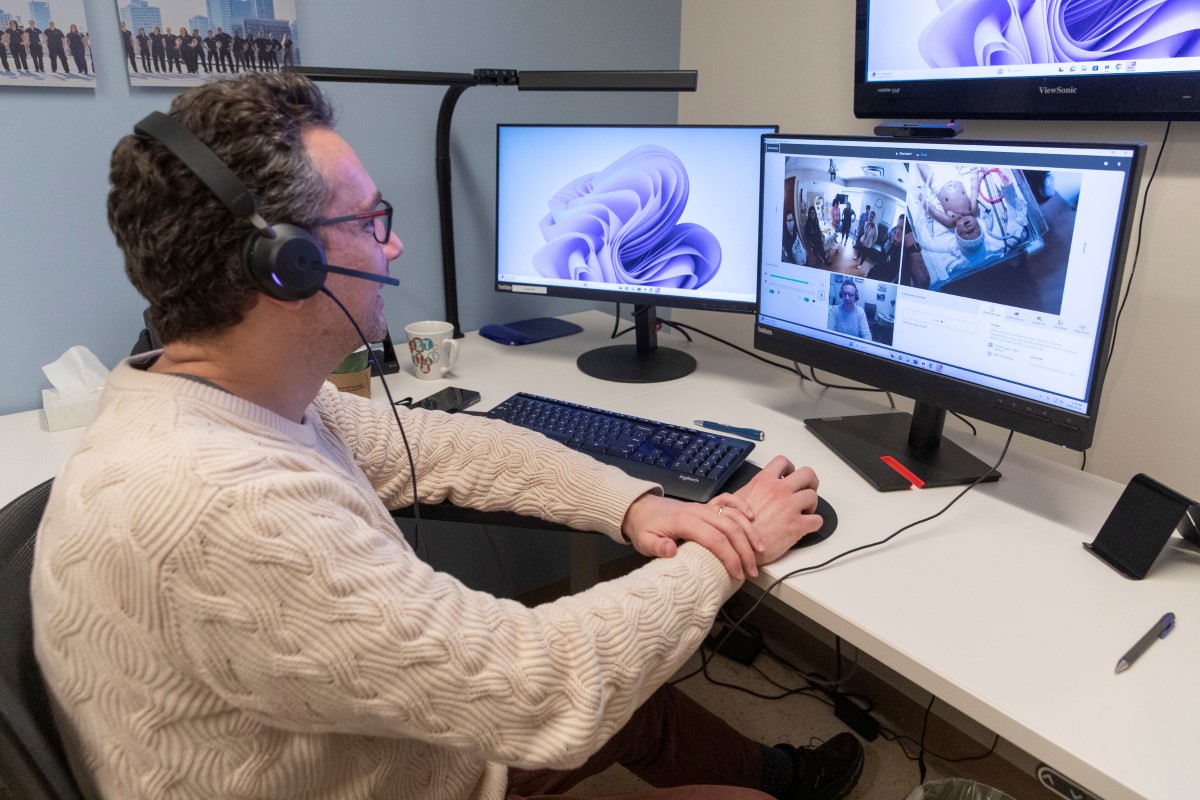 Staff member wearing a headset looks on at simulation session on a screen.