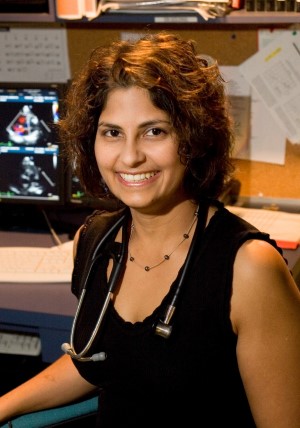 Dipchand, in 2007, wearing a black shirt and stethoscope, smiling in front of a computer showing medical images.