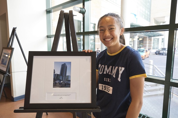 Young girl stands next to her photo, framed and on an easel.