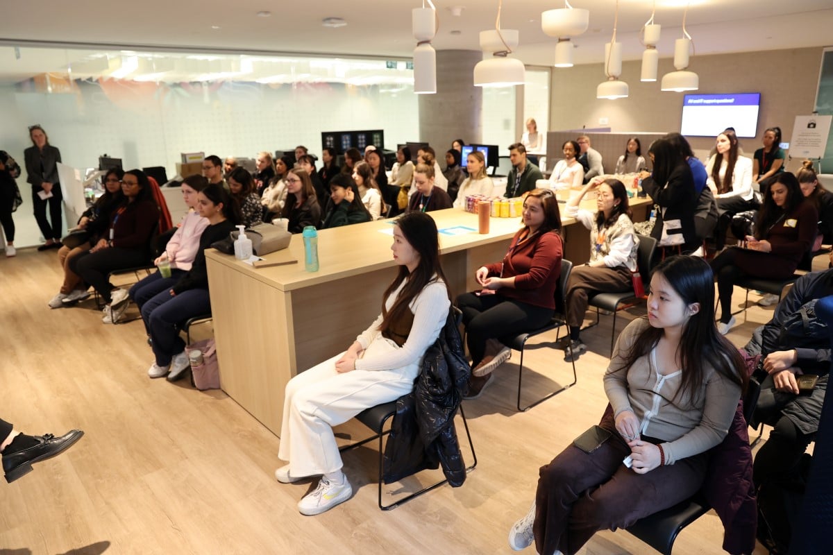 Group seated in a bright room with wooden floors, listening to a presentation.