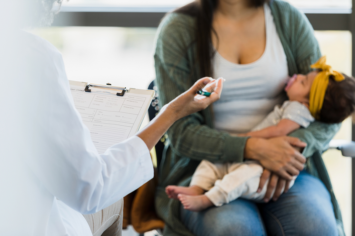 A women holding an infant while a doctor with a clipboard sits in front of them.