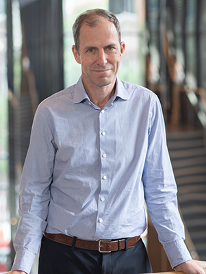 Dr. Peter Dirks stands inside a glass building with his hands on a railing.