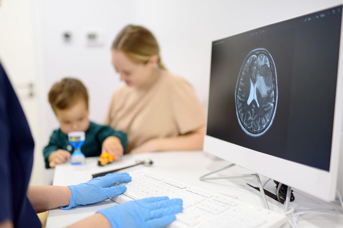 A parent and child sit with a physician examining a scan of the child's brain. 