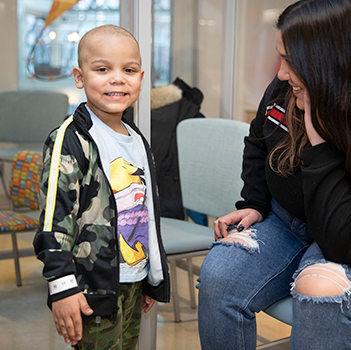 A young boy stands next to his seater mother, smiling at the camera.