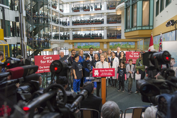 Kathleen Wynne stands on a stage at SickKids in front of reporters