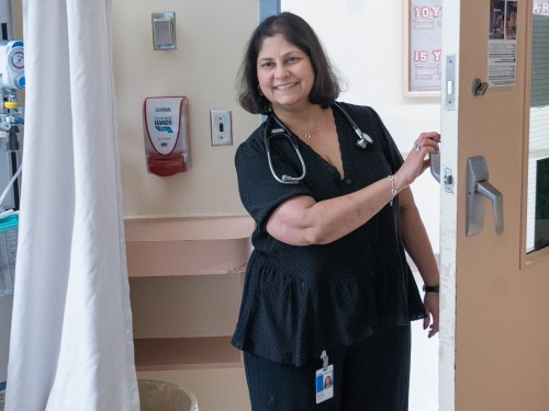 Wearing a black shirt and pants, Dipchand smiles as she knocks on the door of a patient room.