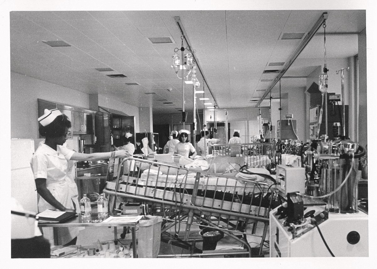 A black and white photograph from 1968 showing a busy hospital room with medical staff attending to patients in the newly opened Paediatric Intensive Care Unit (PICU) at SickKids. The room is filled with medical equipment, and nurses are seen working diligently. 