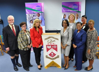 Healthcare professionals gather around Bermuda College crest with "Nursing Pathway" banners during nursing education partnership event.