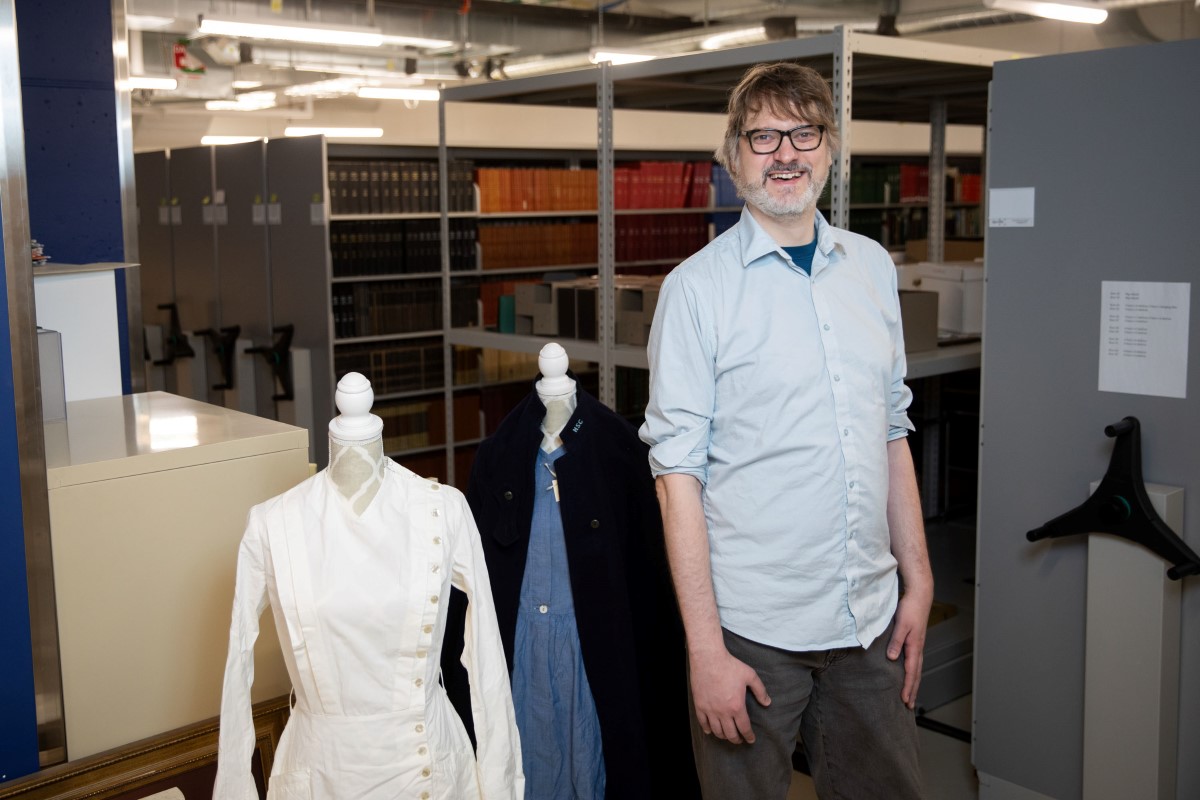 A smiling man in an archives room with historical medical uniforms displayed on mannequins nearby.