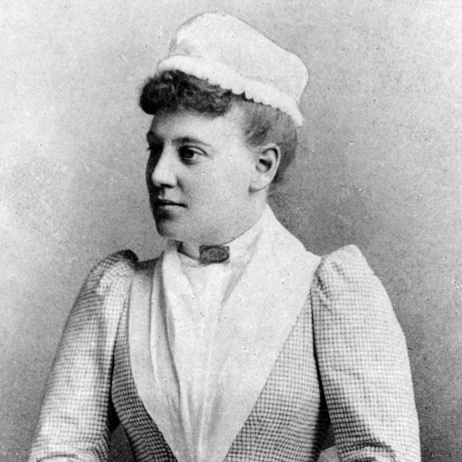 Black and white portrait photograph of a Victorian-era nurse wearing a traditional uniform with checkered dress, white apron, collar, and nursing cap.