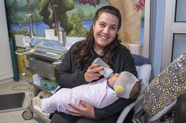 Woman feeds a bottle to an infant who is swaddled.