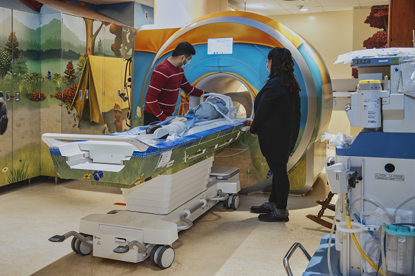 Two adults stand by while a baby is in an MRI scanner.
