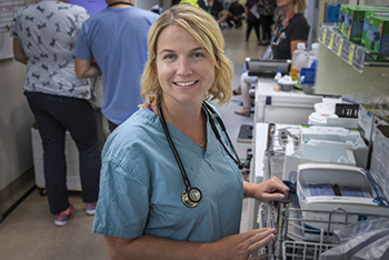 Woman wearing scrubs and a stethoscope stands in a hospital hallway.