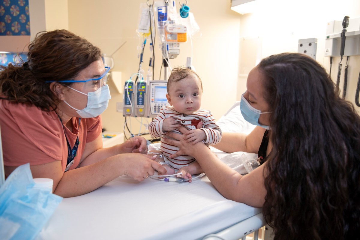 Nurse and parent with a baby on a hospital bed.