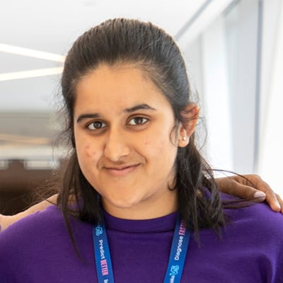 Headshot of young woman wearing a purple t-shirt and SickKids lanyard.