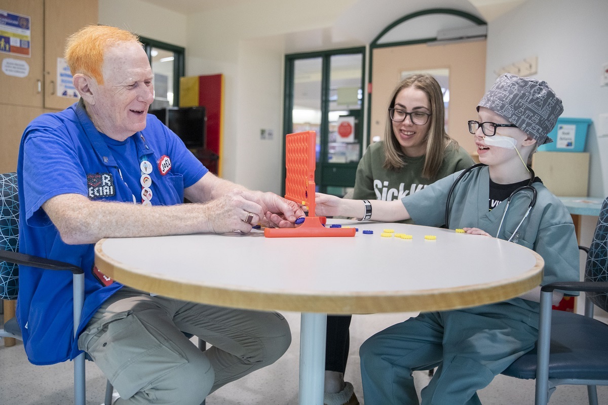 Volunteer plays a board game with a patient and parent.
