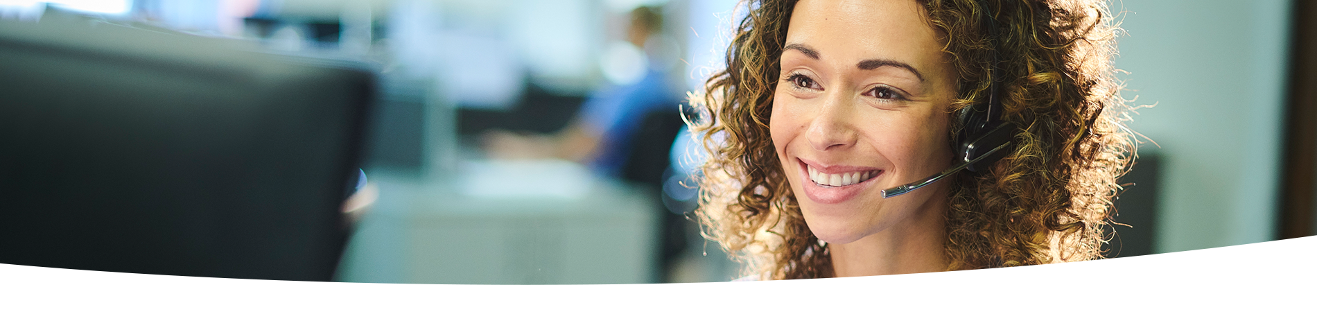 Woman wearing headset and hospital scrubs, seated at a desk.