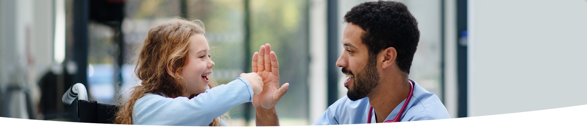 A child in a wheelchair smiling and interacting with a hospital staff member