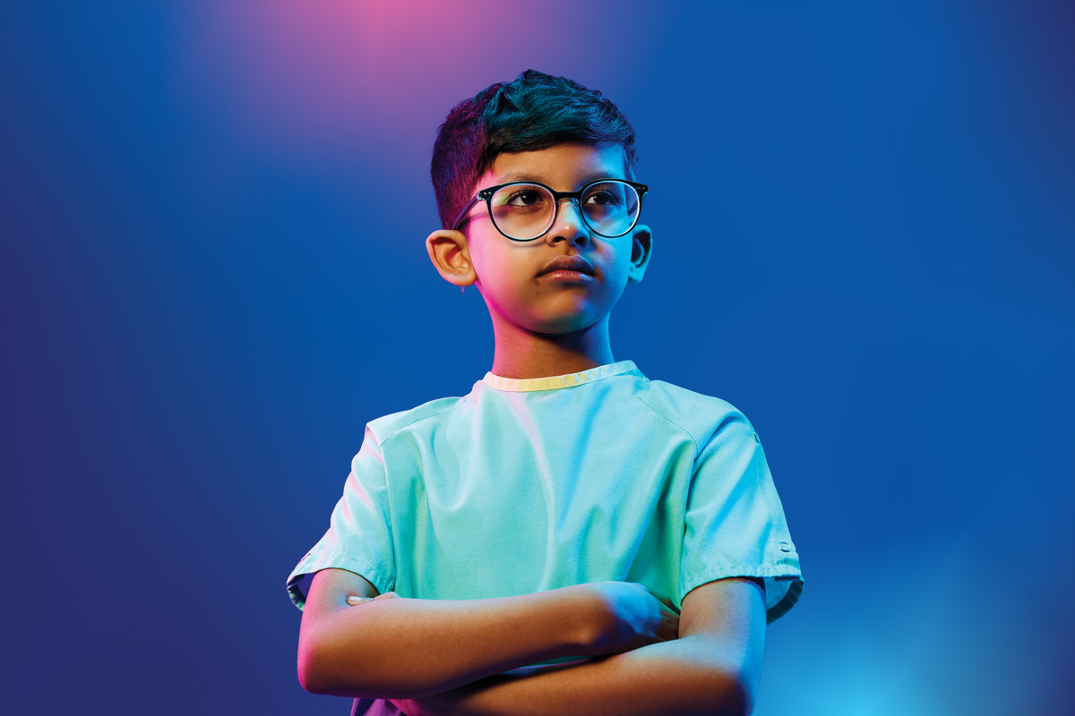 A boy wearing glasses and crossing his arms in front of a blue and pink gradient background.