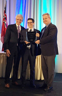 A man in a suit holding a large black plaque with two other men standing next to him