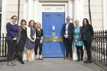 A group of adults stand outside of a large door on a tall white building