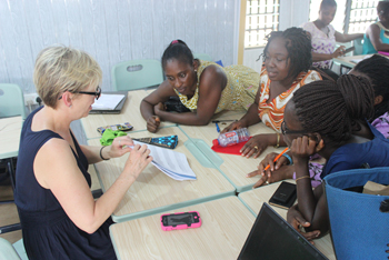 Four women sit at a table. One woman instructs the others with a booklet as the others watch intently