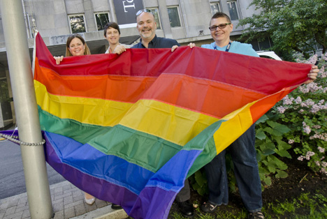A group of four people standing at the bottom of a flag pole holding the Pride Flag at SickKids