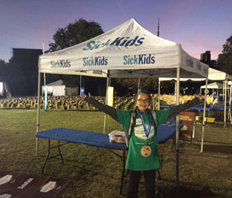 A young girl stands with her hands in the air in front of a SickKids tent