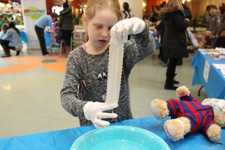 A young girl wearing latex gloves dips a piece of plaster bandage into a bowl of water