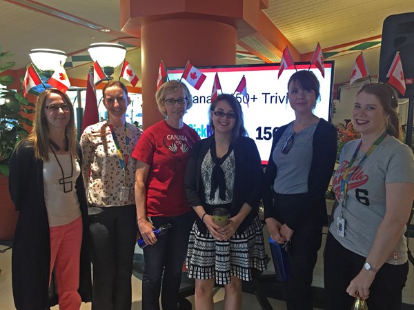 Six women dressed in red and white and each wearing a headband with two Canadian flags sticking out of them.