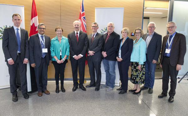 Group of 10 people dresses semi formally stand side by side in front of a podium and flags..