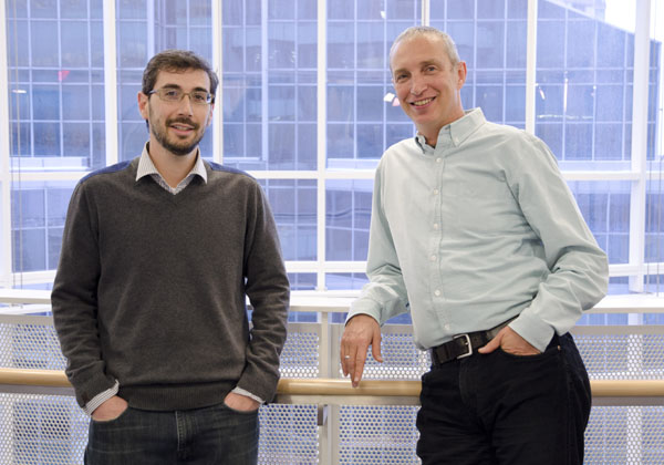 Two men stand leaning against a railing.