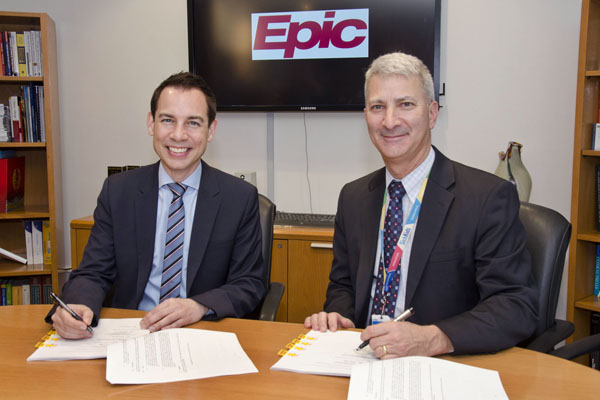 Two men sign papers while seated at a table.