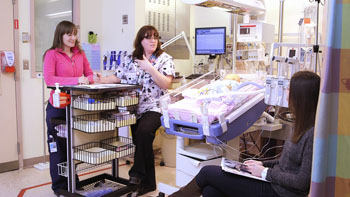 Group of clinicians stand around a hospital bed.