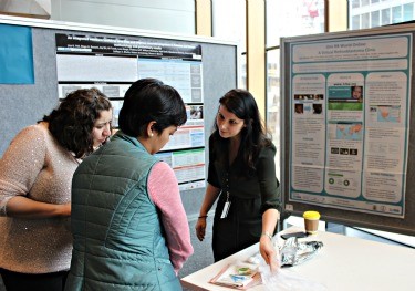Three people stand together, one points at a table. Information boards stand behind them.
