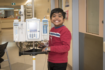 Young boy stands in hallway with IV pump.