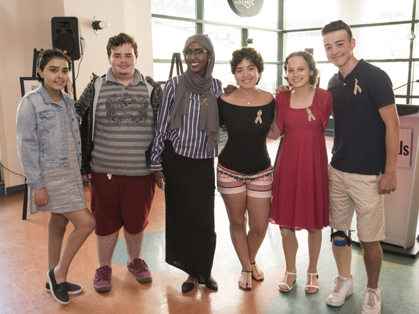 Group of six teens stand arm-in-arm.