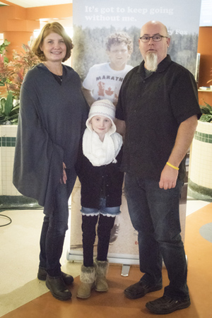 Two adults stand arm in arm with a child standing in between them.