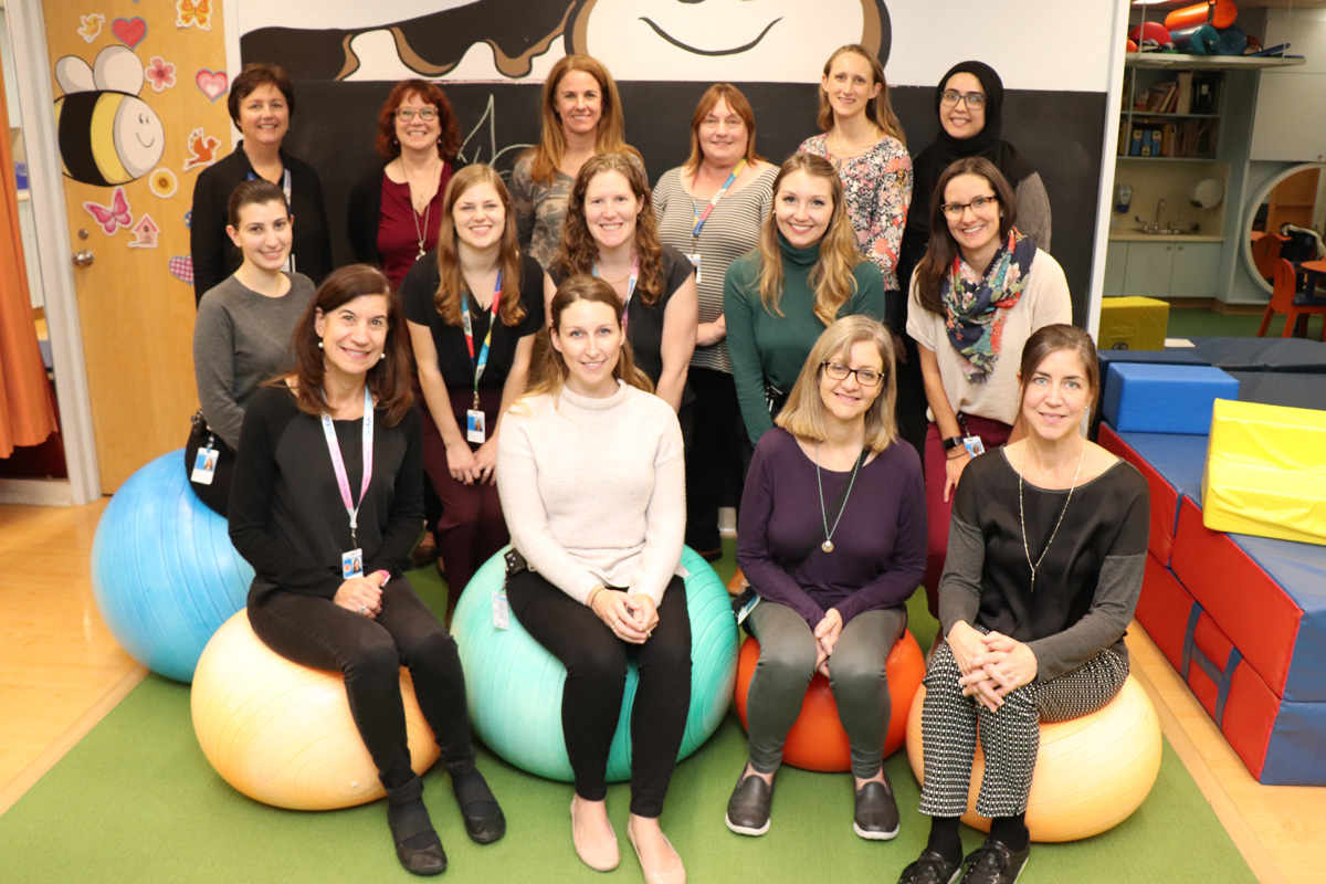 Group of 16 staff gathered in a colourful gymnasium/play area. Front row is sitting on large exercise balls.