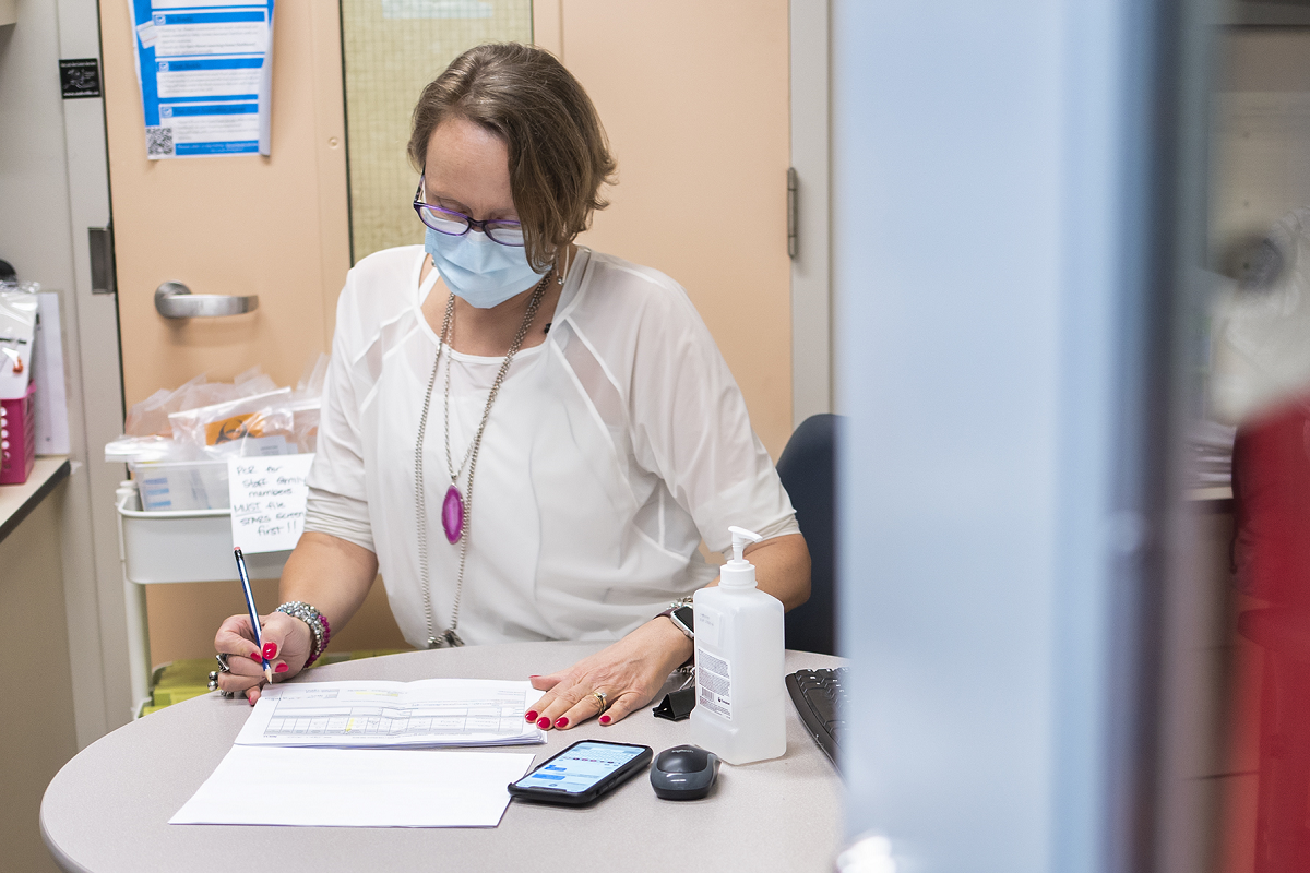 Person seated at a desk reviewing paperwork, wearing a mask.
