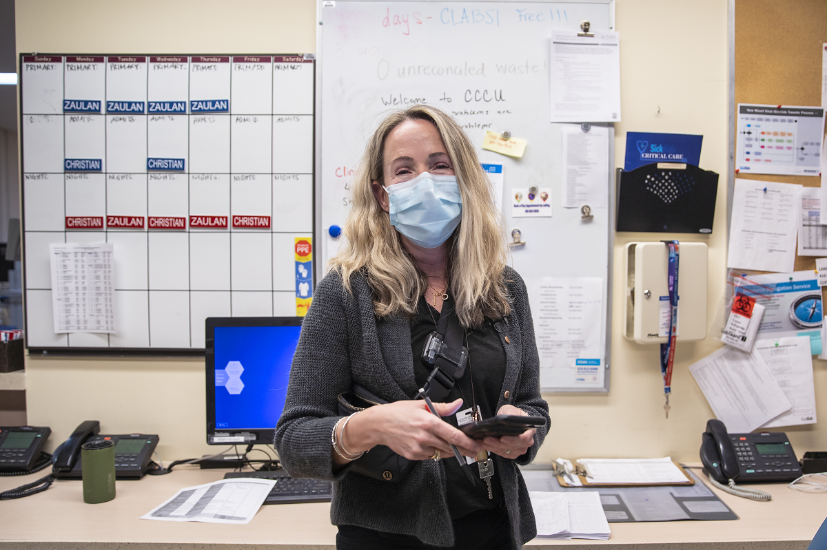Person standing in front of a whiteboard with labels. The person is wearing a mask and holding a cell phone.