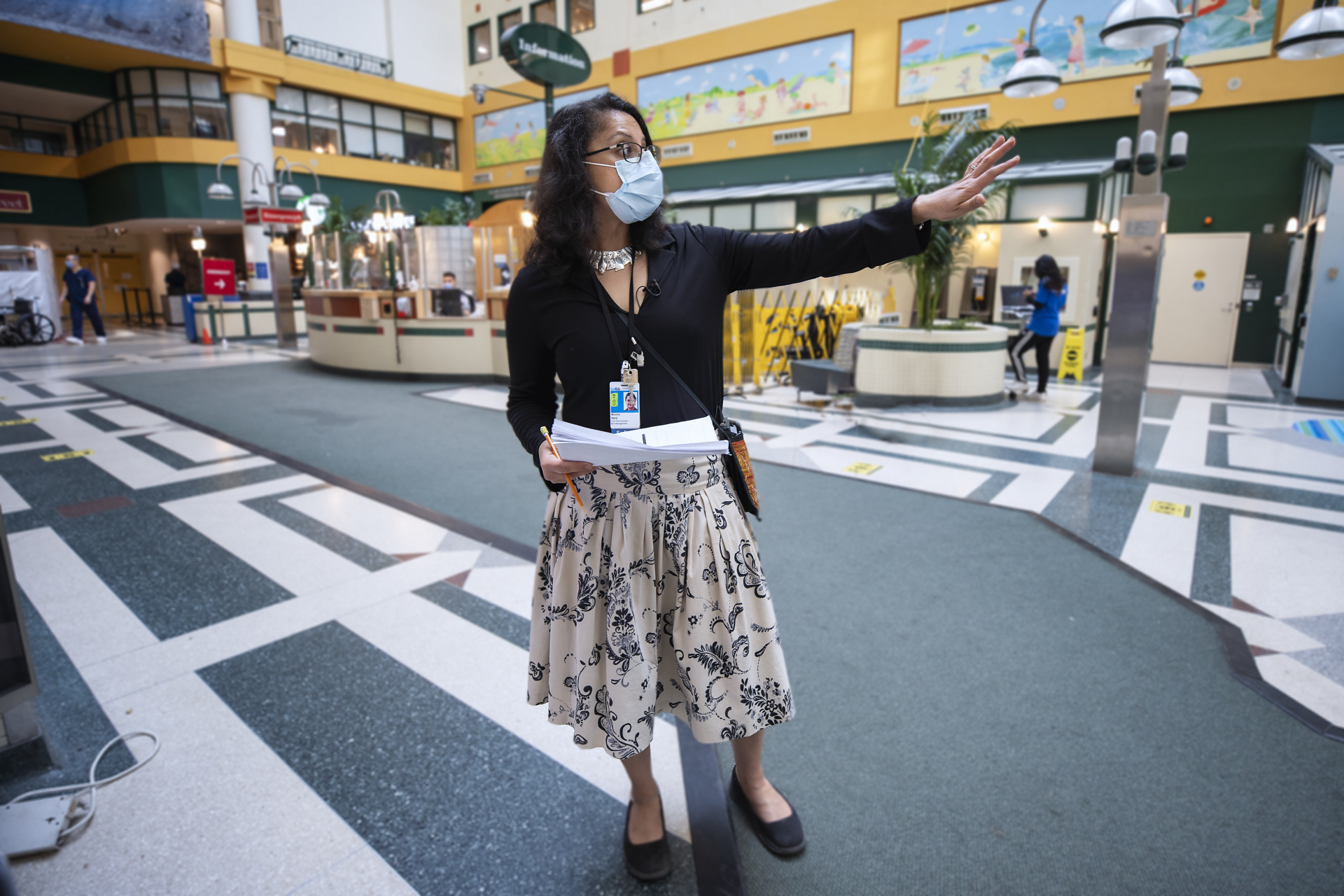Person stands in a lobby area, pointing and holding papers.