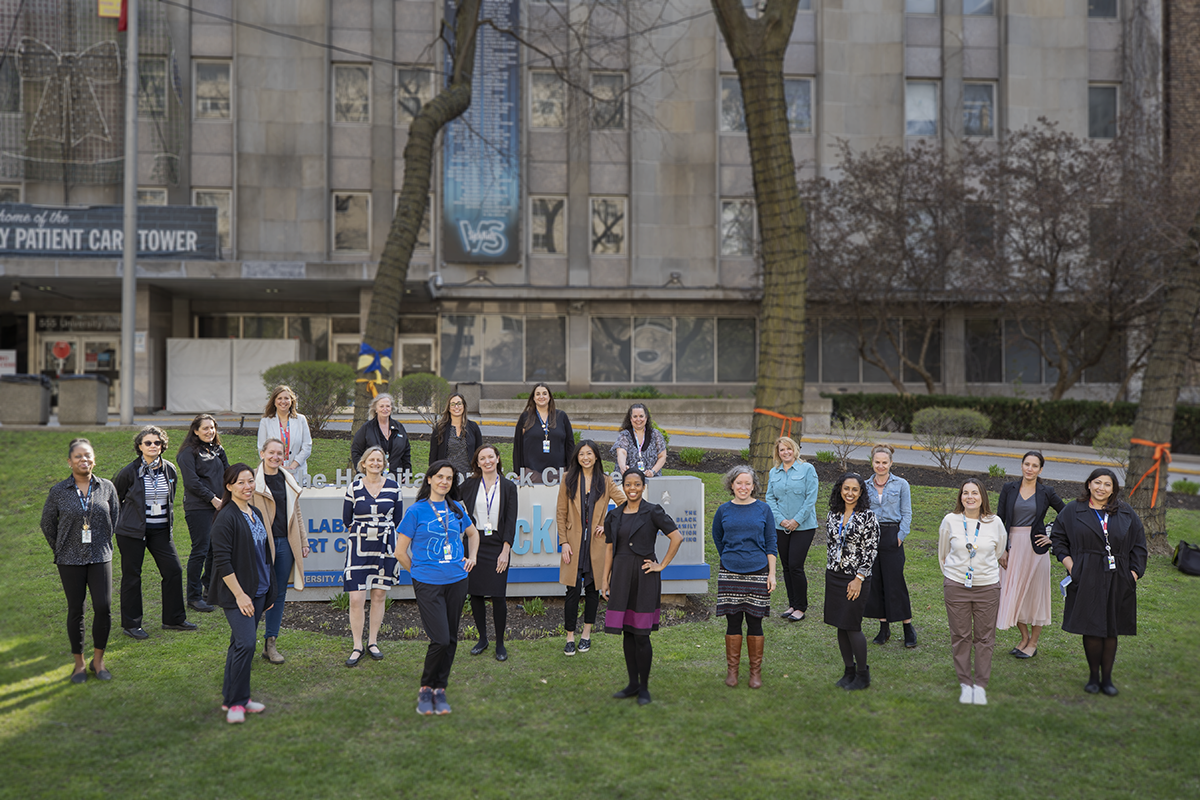 Twenty two women stand together outside SickKids University Ave. side.
