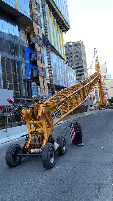 A tall structure made of orange painted metal extends along a city street